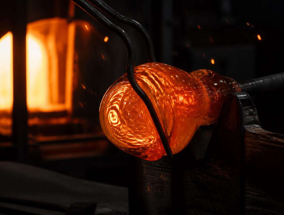 Molten glass gather being shaped with jacks at the furnace